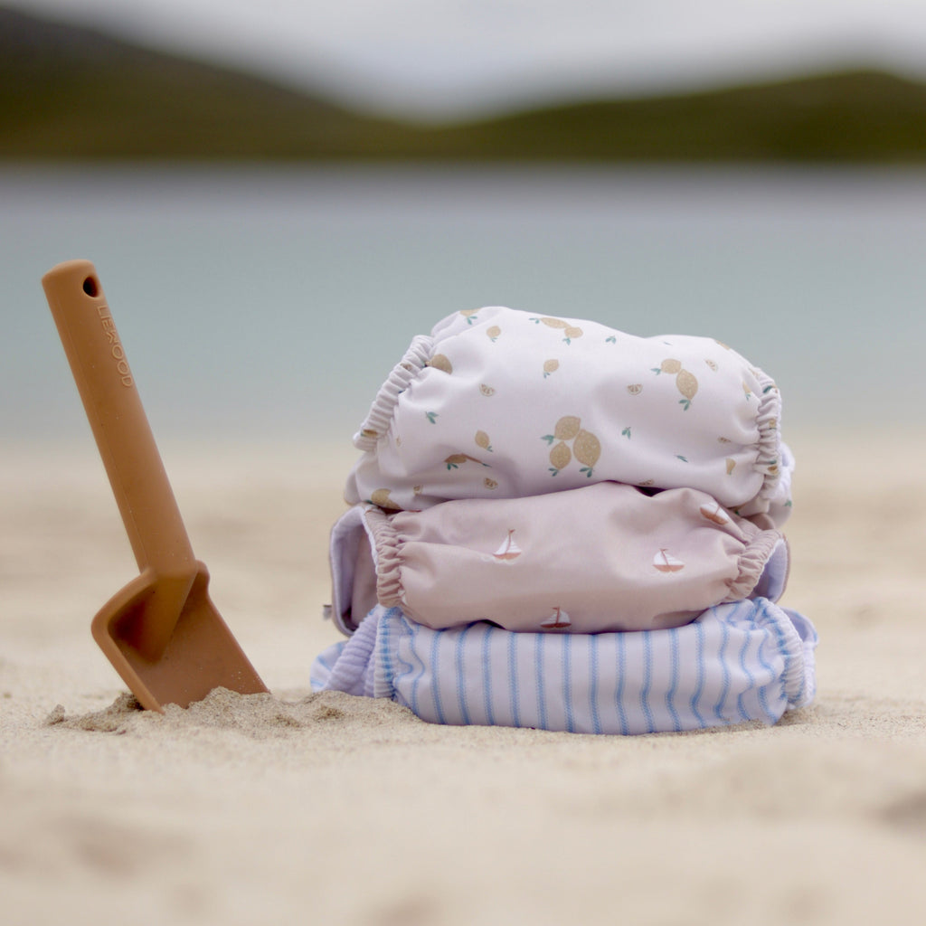 Reusable swim nappies on sand with spade